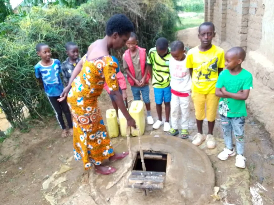 A woman showing children how water is drawn from a covered well
