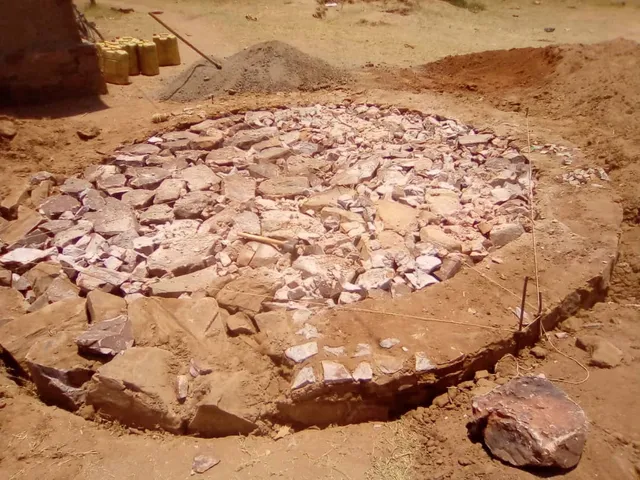A circular stone foundation beside sand, gravel, and water containers